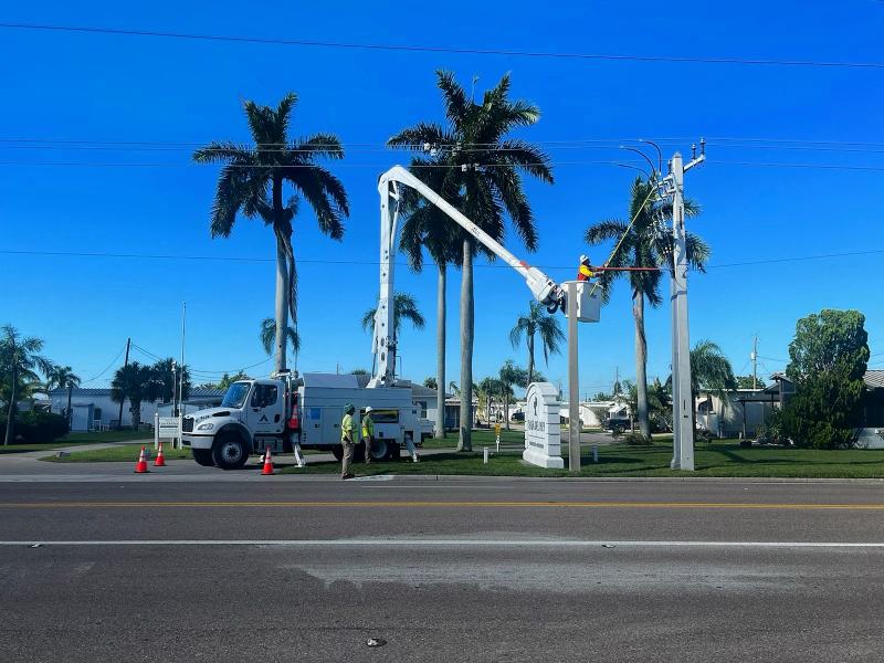 A Bucket Truck in Front of Palm Trees and Power Lines with Men Working After a Hurricane